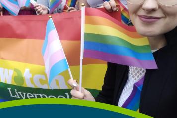 Front cover of the Healthwatch Liverpool Annual Report 2022-23. A Healthwatch Liverpool staff member is taking a selfie while holding a pride flag and trans pride flag in front of colleagues and volunteers holding a larger Healthwatch Liverpool Pride Flag at Liverpool Pride 2022