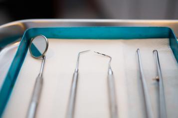 A close up photo of several dentist's tools, including dental probes and a mouth mirror, laid out next to each other.